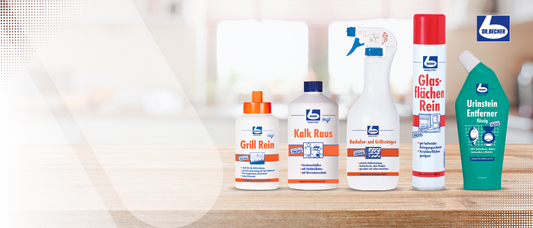 Auf einer Holzoberfläche wird eine Serie von fünf Reinigungsprodukten mit unterschiedlichen Etiketten und Farben präsentiert. Die Produkte sind (von links nach rechts) Grill Rein, Kalk Raus, eine Sprühflasche, Glasflächen Rein und Urinstein Entferner. In der oberen rechten Ecke ist ein Logo zu sehen.