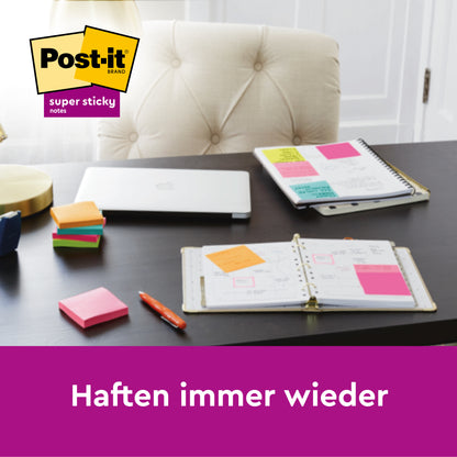 Ein Schreibtisch mit den Post-it® Super Sticky Notes im Großformat (101 mm x 101 mm, 90 Blatt/Block, 100% PEFC) der 3M Deutschland GmbH, Notizbüchern, einem geschlossenen Laptop, einem Stift und bunten Notizblöcken. Unten steht: "Haften immer wieder.