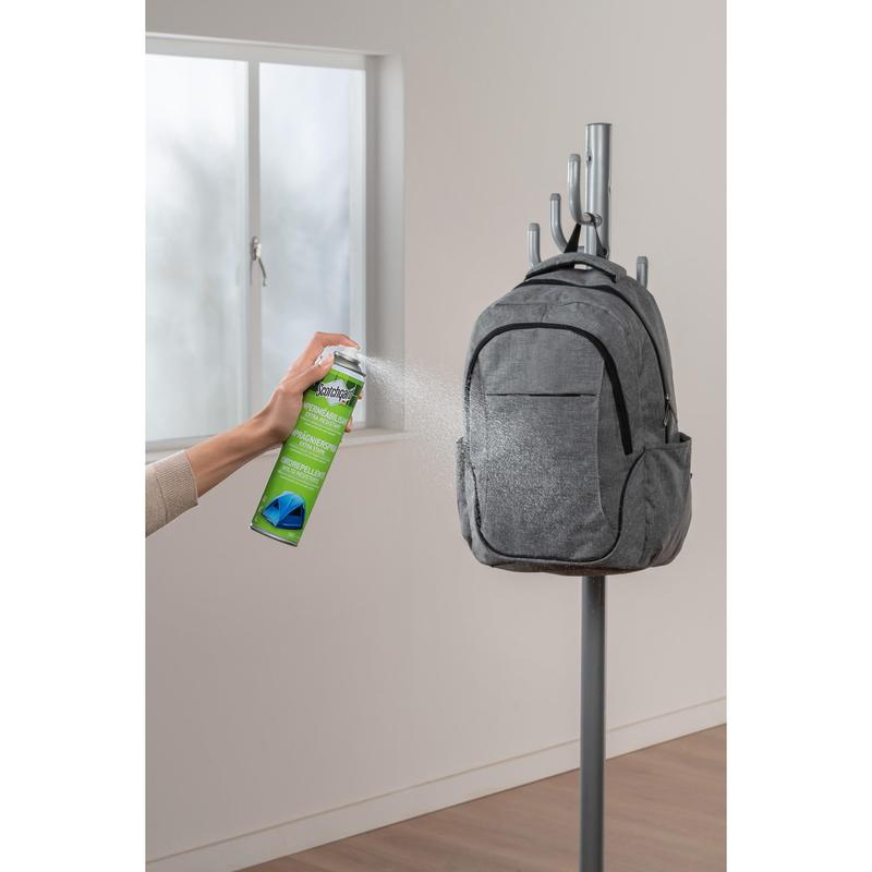 A hand sprays Scotchgard™ Heavy Duty Water Shield, 400ml from 3M Deutschland GmbH onto a gray backpack on the coat rack to provide strong waterproof protection for textiles.