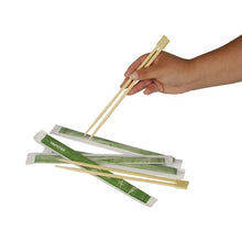 A hand holds wooden PAPSTAR chopsticks "pure" 23 cm over several pairs, each individually wrapped in green paper sleeves. Product: PAPSTAR chopsticks "pure", 50 pairs | Film by PAPSTAR GmbH, depicted on a white background.