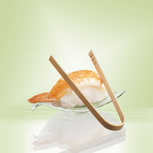 A shrimp nigiri sushi is served on a glass dish, complemented by PAPSTAR bamboo finger food tongs (10 cm, 50 pieces) from PAPSTAR GmbH. A gentle light green highlights the eco-friendly bamboo presentation.
