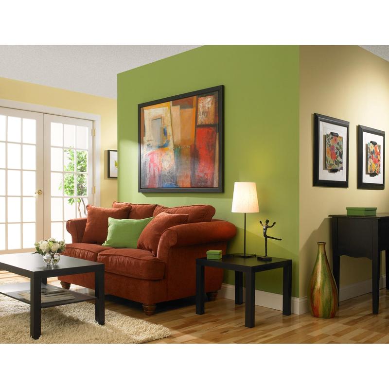 A living room with yellow and green walls painted with ScotchBlue™ Painter's Tape "Multi-Surface" by 3M Deutschland GmbH, a red sofa with green cushions, a black coffee table, a side table with a lamp, abstract art, wooden flooring, and glass doors.