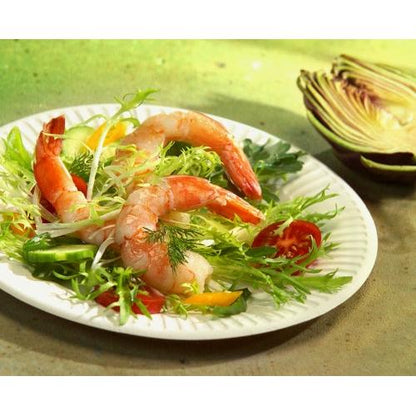 A PAPSTAR 100 plates, cardboard "pure" round, white extra strong from PAPSTAR GmbH holds a salad with leafy greens, shrimp, cucumbers, yellow peppers, cherry tomatoes, and dill. In the background, a sliced red cabbage head lies on a green surface.