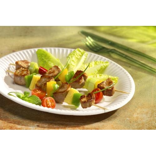 A PAPSTAR paper plate round Ø 26 cm, extra strong, white "pure" by PAPSTAR GmbH holds two skewers with grilled meat, cherry tomatoes, cucumber slices, and yellow pepper on salad and mint; green plastic cutlery in the background.