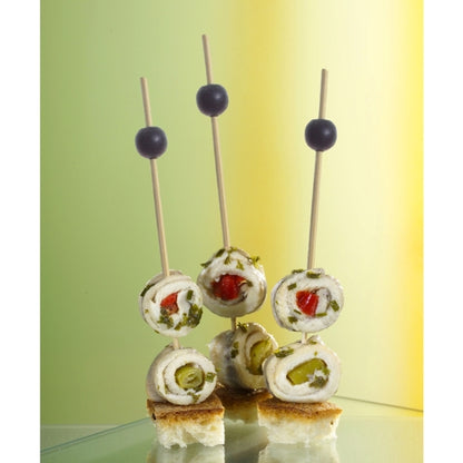 Three PAPSTAR 250 finger food picks from PAPSTAR GmbH hold cheese, herb, and vegetable rolls on bread cubes, each garnished with a black olive. The softly lit background is in green and yellow tones.