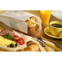 A breakfast spread with cheese slices, cold cuts, olives, tomatoes, and parsley on a wooden board; a croissant; PAPSTAR 1000 paper folding bag rolls from PAPSTAR GmbH; coffee; orange juice; and cutlery on a wooden table.