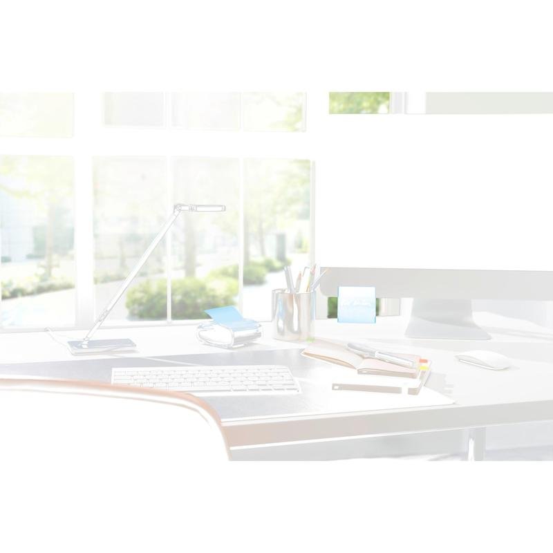 A modern desk setup with a 3M Post-it® Z-Notes Dispenser PRO in black with yellow Post-it® Super Sticky Z-Notes (76x76 mm, 90 sheets/block), notebooks, pens, and a lamp in front of large windows with sunlight and green trees outside.