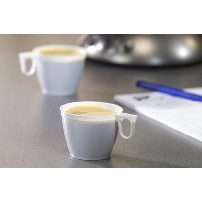 Two white Starpak 60 coffee cups (0.18 l, PS, Ø 7.8 cm, 6 cm), one in focus and one blurred in the background, are placed on a gray surface, with a pen and paper partially visible on the right side.