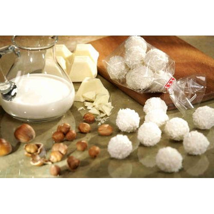 On a counter, there is a glass jug with milk, white chocolate chips, hazelnuts, and coconut candies next to a Starpak 300 flat-bottom bag, a transparent PP bag from Starpak, filled with various treats.