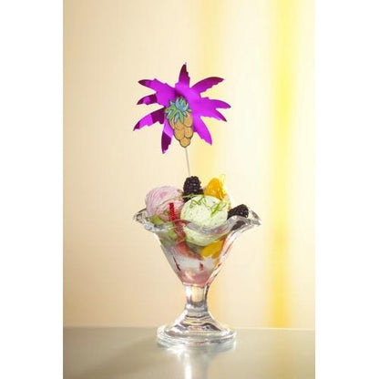 A glass dessert bowl with glowing ice, fruits, and blackberries is elegantly decorated with a decorative pick "Palm Leaves" 19.5 cm (assorted colors) by PAPSTAR GmbH from the 50-piece cardboard tray set against a soft yellow background.