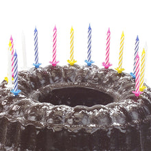 Ein Schokoladenkuchen mit Puderzucker bestreut und dekoriert mit zehn PAPSTAR Geburtstagskerzen 6 cm, farbig sortiert mit Halter (von PAPSTAR GmbH) in verschiedenen Farben.