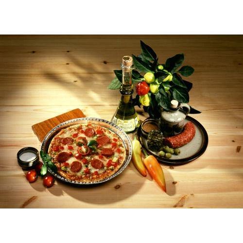 A pepperoni pizza lies on a plate next to white wine, sausage, and olives – freshly baked in Starpak 25 round molds aluminum round by Starpak for optimal heat conduction – accompanied by tomatoes, peppers, and a potted plant on a wooden table.