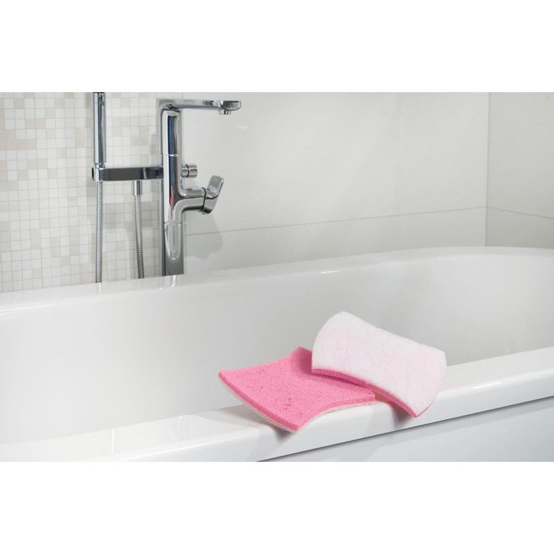 Shown is a white bathtub with chrome fittings. On the edge are a pink bathroom sponge and a Scotch-Brite® Bath XXL cleaning sponge for the bathroom from 3M Deutschland GmbH. The background shows white tiles with a mosaic pattern.