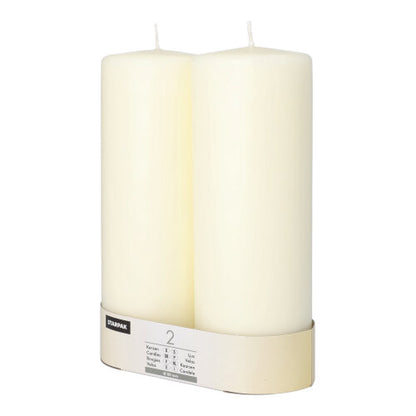 Two unlit Starpak 2 pillar candles Ø 80 mm with flat top stand side by side, wrapped at the base with a labeled band, exuding timeless elegance.