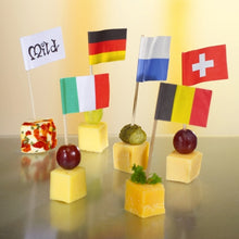 Six cheese cubes are topped with grapes or herbs and decorated for a stylish and eco-friendly presentation with the 8 cm large white deco-picker flags from PAPSTAR GmbH, with each flag labeled "Mild", Germany, Italy, Finland, Switzerland, or Belgium.