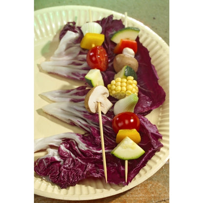 Two vegetable skewers on PAPSTAR 250 bamboo skewers, "pure" (PAPSTAR GmbH), filled with mushrooms, tomatoes, corn, zucchini, onions, and bell peppers, lie on large radicchio leaves on a paper plate.
