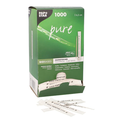 A partially opened PAPSTAR toothpick "pure" dispenser box (1000 pieces) of PAPSTAR GmbH shows 6.5 cm round wooden toothpicks that are individually wrapped; in front are several white-wrapped toothpicks.