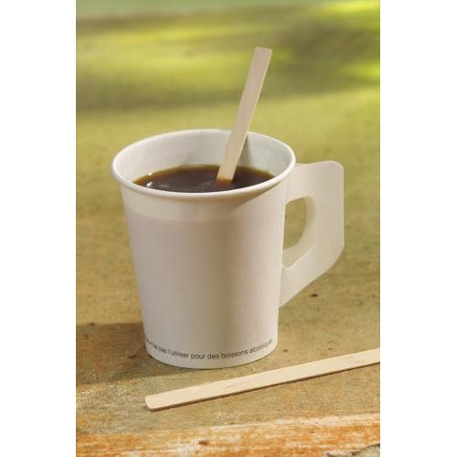 A white paper cup with dark coffee and a PAPSTAR "pure" stirring stick from PAPSTAR GmbH stands on a shelf; next to it lies another wooden stirring stick. The naturally light background is gently blurred.