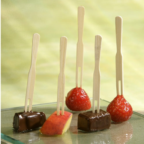 On five PAPSTAR finger food skewers "pure" (8.5 cm) from PAPSTAR GmbH, two strawberries, two chocolate cubes, and an apple slice are skewered, presented upright on a glass against a light green background.