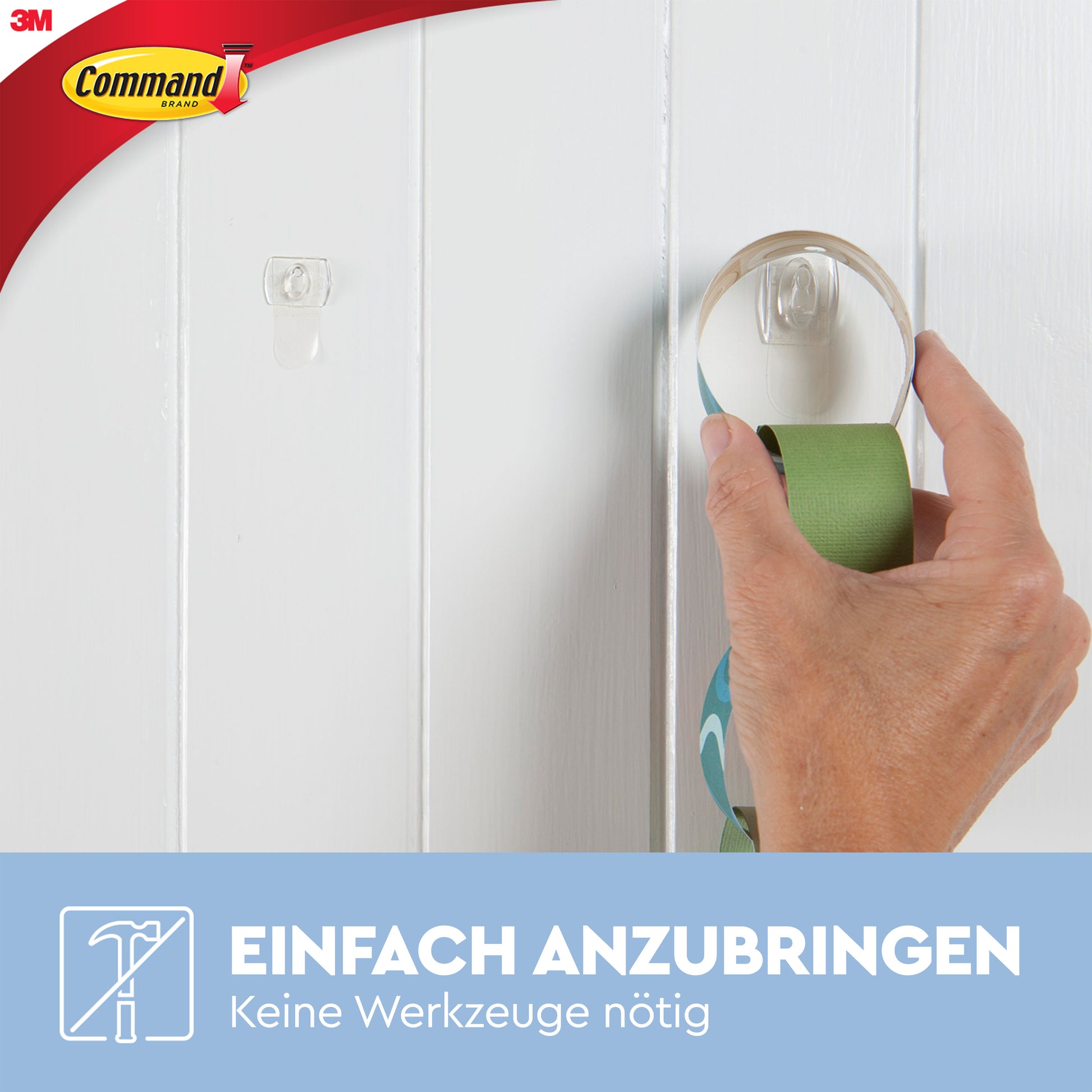 Eine Hand befestigt einen Command™ Mini-Haken, transparent, mit transparenten Strips (3M Deutschland GmbH) an einer weißen Holzwand. Text unten: "Einfach anzubringen. Keine Werkzeuge nötig.