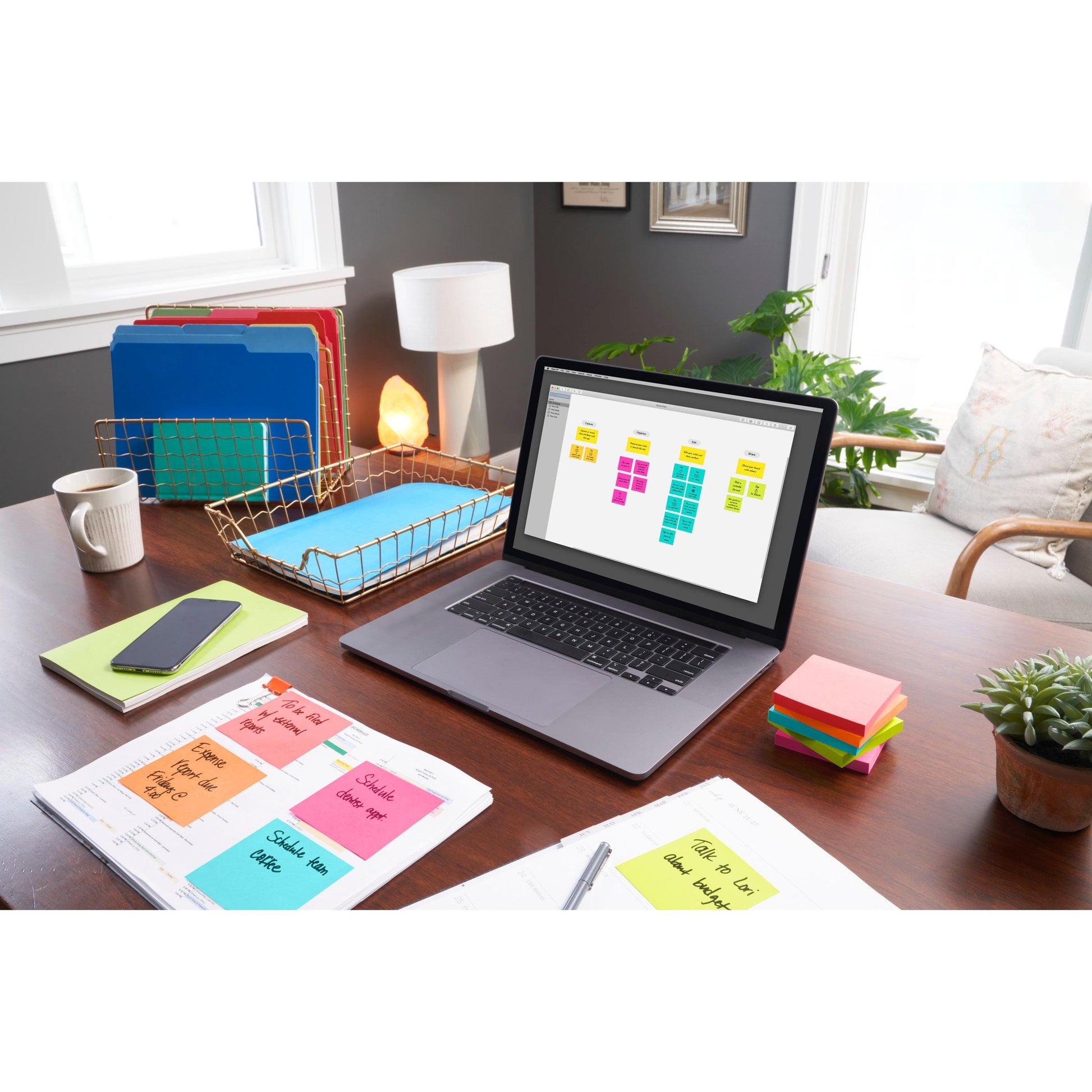 Ein Schreibtisch mit einem Laptop, auf dem ein Haftnotiz-Organizer, Post-it® Notes (76 mm x 76 mm, 100 Blatt/Block, 100% PEFC) von 3M Deutschland GmbH, Ordner, Papierkram, ein Telefon, eine Lampe, eine Pflanze und Sonnenlicht den organisierten Arbeitsbereich erhellen.