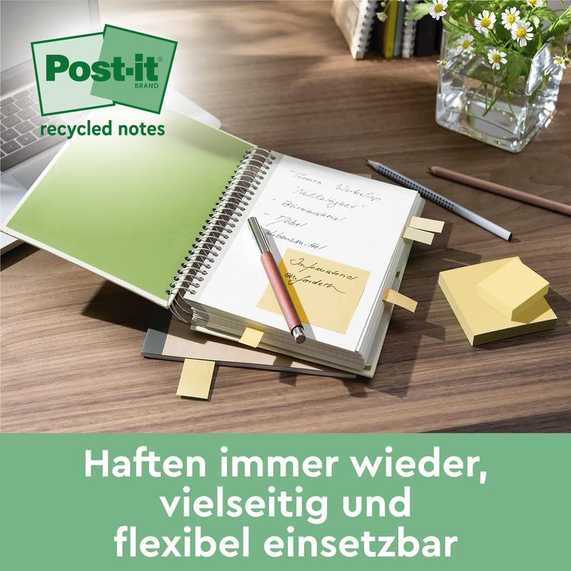 On a desk lie a Post-it® Recycling Z-Notes pad (76x76mm, 100 sheets, 100% PEFC) by 3M Deutschland GmbH, sticky notes in an open notebook, a pen, scattered notes, a glass of water, and a potted plant. "Stick again and again - versatile & flexible.