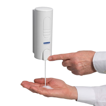 A person dispenses Kimberly-Clark Scott® ESSENTIAL™ foam soap (pink, 200ml cartridge) from a white, wall-mounted dispenser by pressing the button of the soap cartridge with one hand and catching the foam in the other palm.