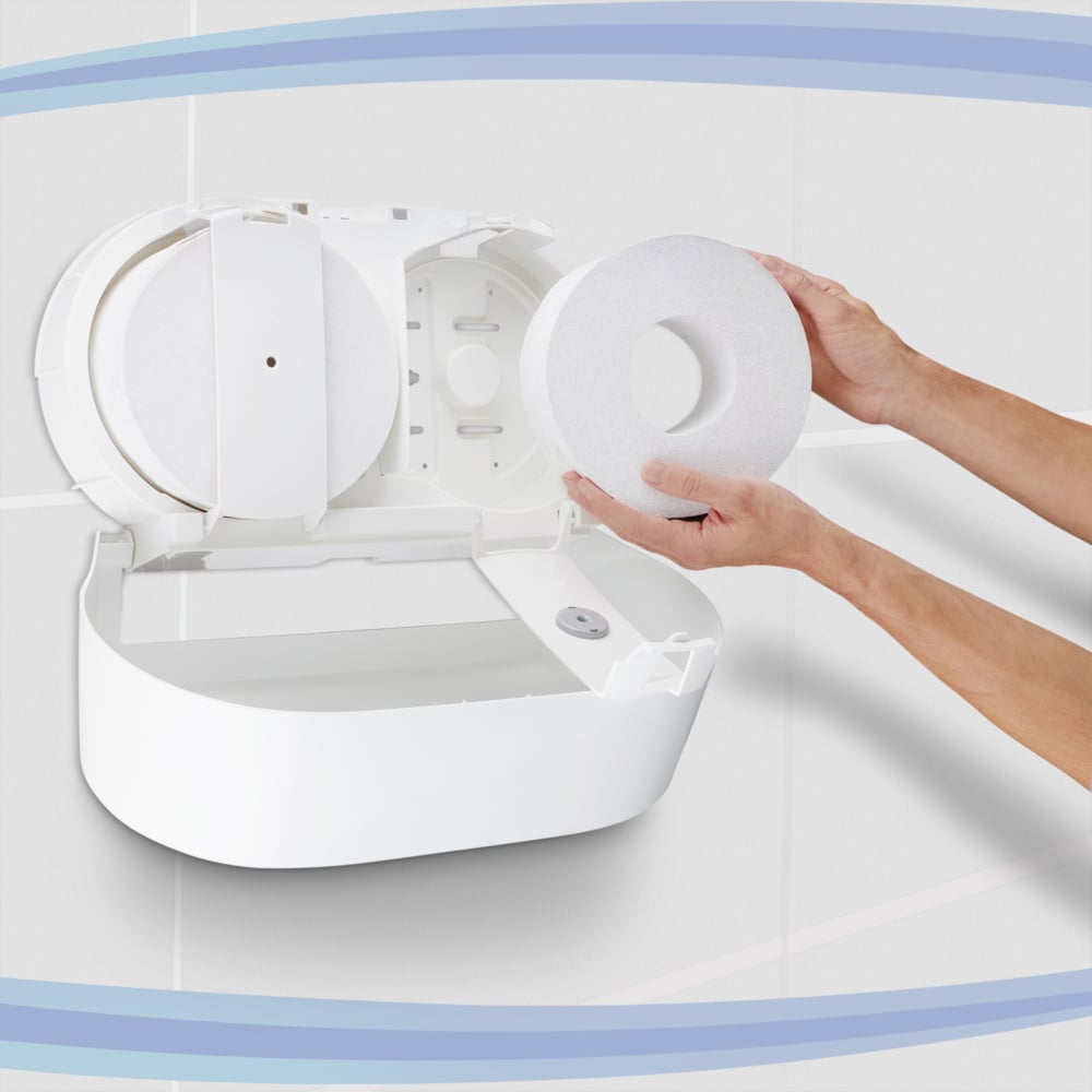 A person loads a Kimberly-Clark GmbH Aquarius™ toilet paper dispenser - central pull / white / Jumbo, with the lid open. The white tiled walls and blue curves in the background highlight the practical central dispenser design.