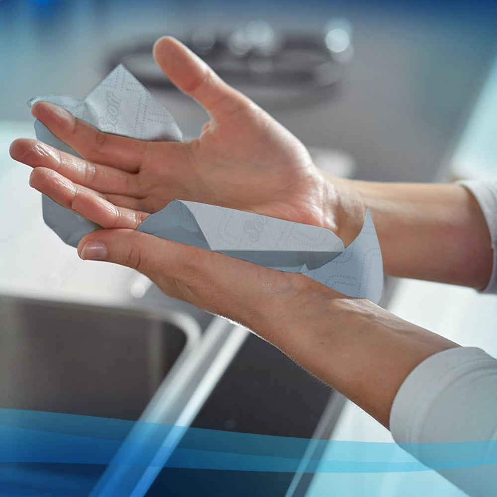 A person dries their hands with Scott® Essential™ towels from Kimberly-Clark GmbH (roll / blue - 6 rolls) over a sink in a modern kitchen.