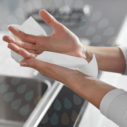A person dries their hands over a sink with Kleenex® folded hand towels - White/Large (15 clips x 124 sheets | box) by Kimberly-Clark GmbH, with both hands and part of the sink visible in the background.