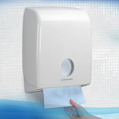 A hand pulls a blue Scott® Control™ Interfold Hand Towel from a white dispenser from Kimberly-Clark GmbH, with the box containing 15 packs of 240 sheets each, against a tiled background.