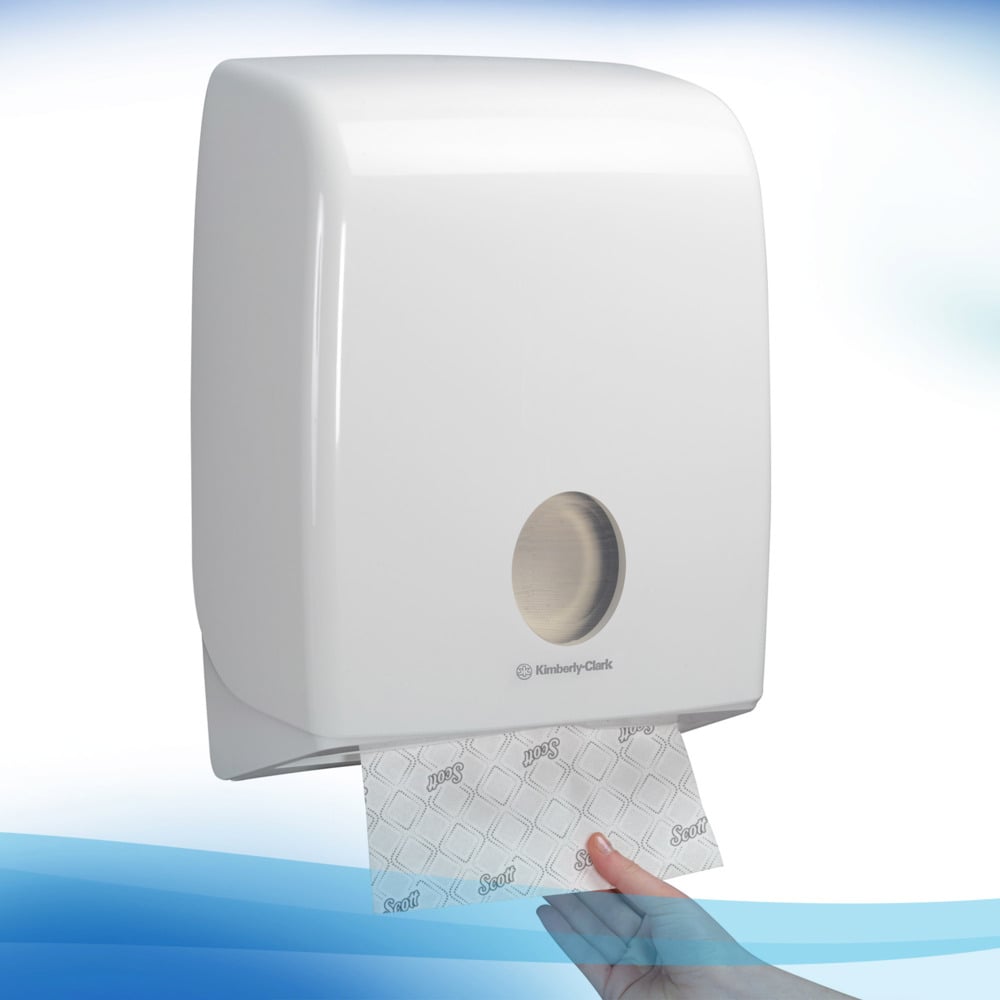 Ein weißer, wandmontierter Spender der Kimberly-Clark GmbH spendet ein einzelnes Blatt Scott® Handtücher - Narrow-Fold / Weiß durch die metallene Frontöffnung und sorgt so für hygienische Händetrocknung bei jedem Zug.