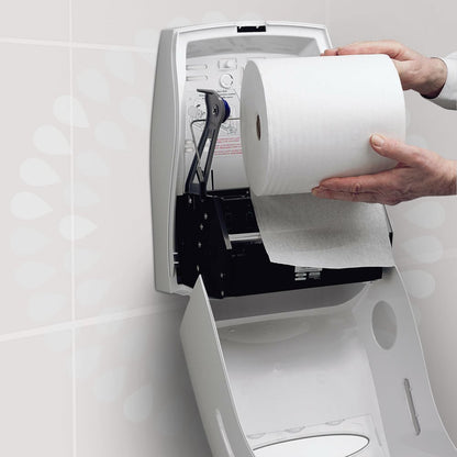 A person loads a Kleenex® Ultra™ hand towel roll from Kimberly-Clark GmbH into a white, open wall dispenser in a toilet to ensure hygienic hand drying. Instructions are printed on the lid of the dispenser.