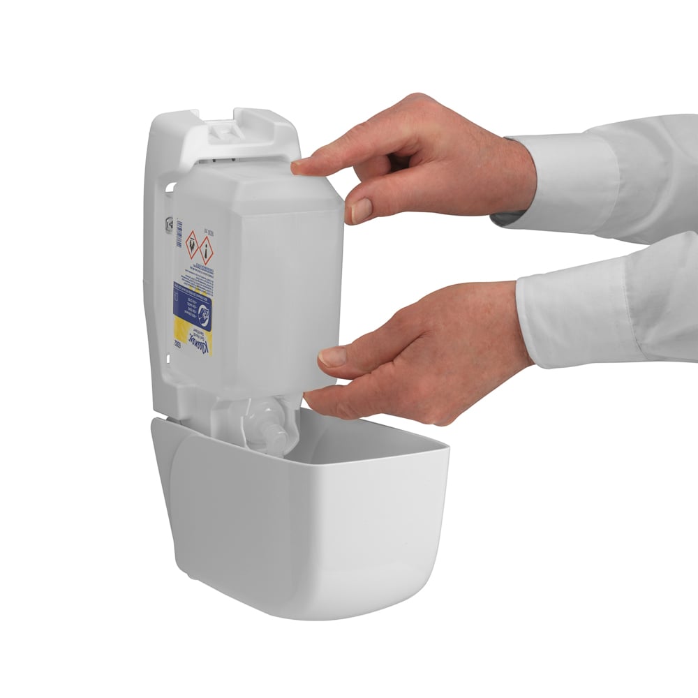 Eine Person füllt einen an der Wand montierten Spender der Kimberly-Clark GmbH Kleenex® Extra Gel Händedesinfizieren nach, indem sie mit beiden Händen eine neue transparente 1-Liter-Kassette einlegt; durch die offene Vorderseite sind nur ihre Hände und Unterarme sichtbar.