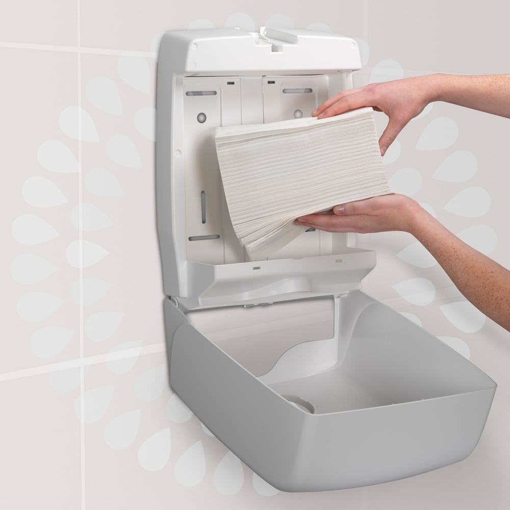 Eine Person lädt einen Stapel Kimberly-Clark GmbH Kleenex® Ultra™ Handtücher MultiFold (Weiß, Klein, 18 Clips x 150 Blatt) in einen wandmontierten Papierhandtuchspender in einer Toilette.