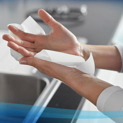 Someone dries their hands with Scott® Control™ Hand Towels - Interfold / White / Small from Kimberly-Clark GmbH, with a kitchen counter and a faucet in the background. The package contains 15 x 304 sheets per carton.