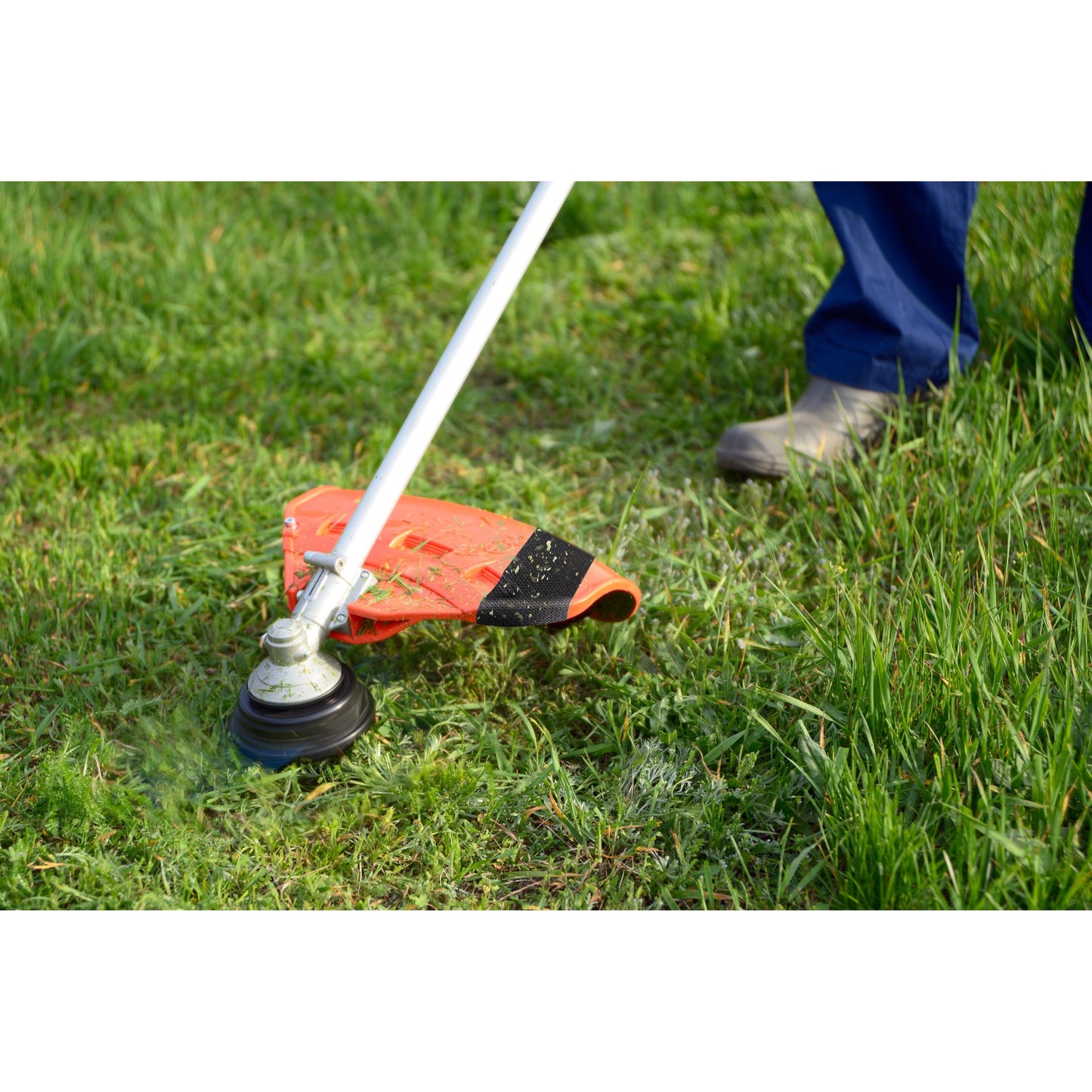 With sturdy boots, a person trims the green grass in the garden, while a roll of Scotch® Extremium™ Ultra High Performance Tape DT17 (10 m x 24 mm) by 3M lies nearby, ready for demanding repairs.