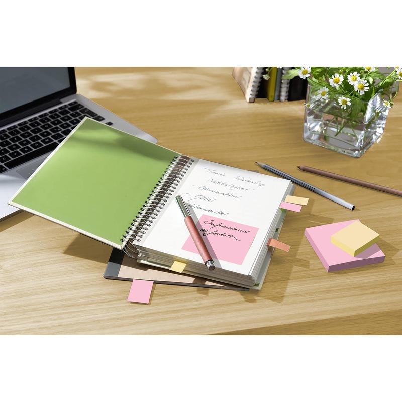 A spiral notebook with handwritten notes, a pen, a laptop, a pencil, and Post-it® Recycling Notes (38x51mm, 100 sheets/block, 100% PEFC) from 3M Germany GmbH on a desk; in the background, a glass vase with white daisies.