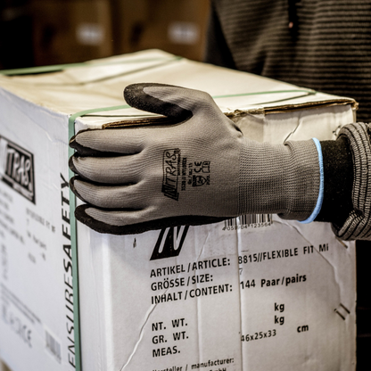 A person wearing Nitras Nylotex nylon gloves with latex coating from AS Arbeitsschutz GmbH holds a large white box with German and English labeling in their hand; only their upper body and arm are partially visible.