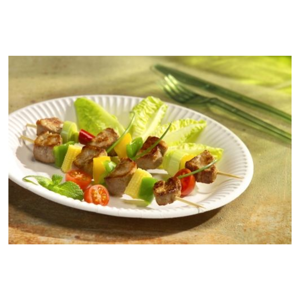 A 29 50 Plate, cardboard "pure" round - white from PAPSTAR GmbH holds skewers with sausage, cheese, cucumber, and tomato on lettuce; in the background, green utensils provide an eco-friendly touch.