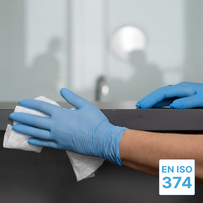 A person wearing ARNOMED NITRIL BLUE XTRA STRONG disposable gloves from ARNOWA GmbH wipes a dark countertop with a white cloth. The EN ISO 374 symbol is visible, a blurred office environment appears in the background.