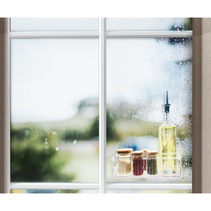 Ein Fenster mit Regentropfen zeigt eine Szene im Freien. Auf der Fensterbank stehen eine Flasche Öl, drei kleine Gläser mit goldenen Deckeln und eine Rolle Scotch-FIX™ Transparentes doppelseitiges Montageband 4910C der 3M Deutschland GmbH.