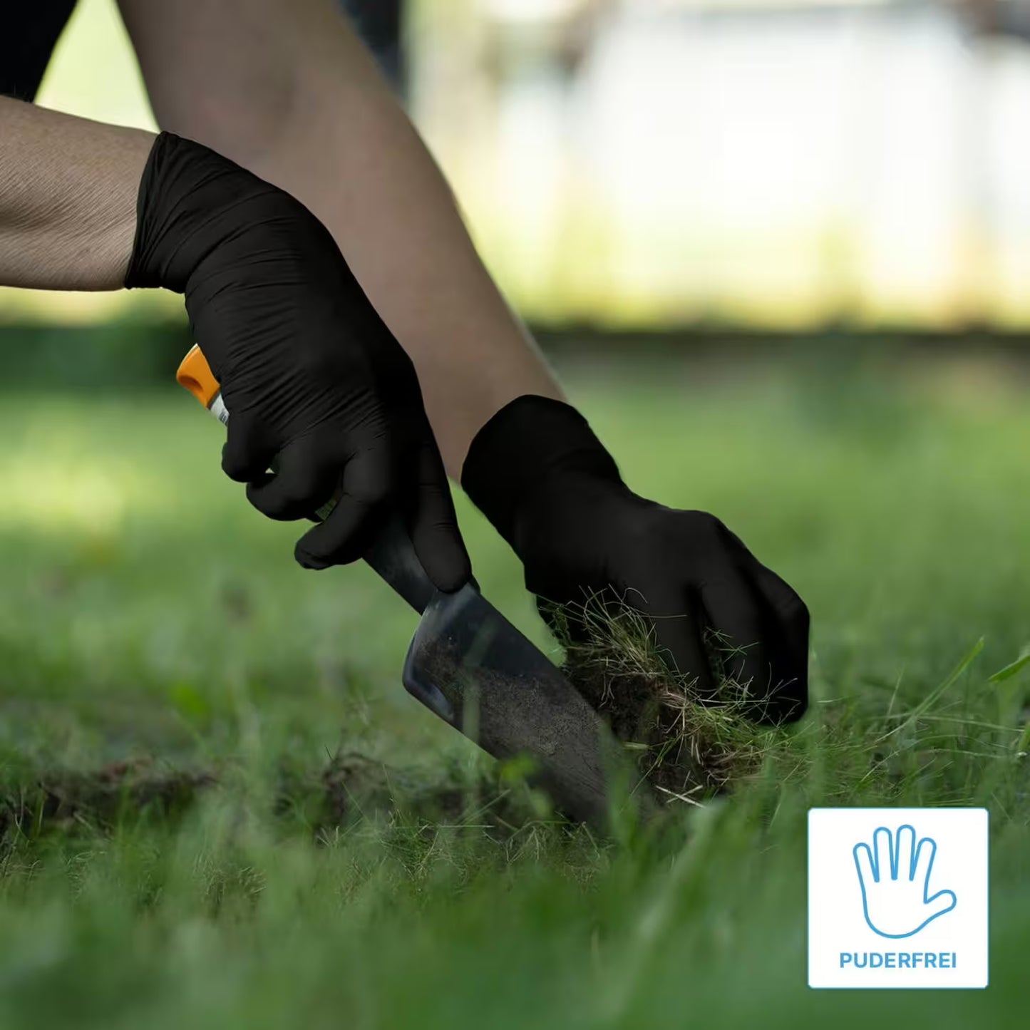 A person wearing ARNOMED NITRIL XTRA PURE BLACK disposable gloves from ARNOWA GmbH uses a small trowel in grassy soil. A "POWDER-FREE" logo with a hand symbol appears in the bottom right.