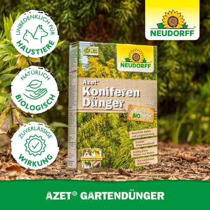 A box of Neudorff Shop Azet Conifer Fertilizer stands outdoors on the ground among green conifers. The German packaging highlights its natural, organic, and pet-friendly properties, making it ideal for evergreen plants and privacy screens.