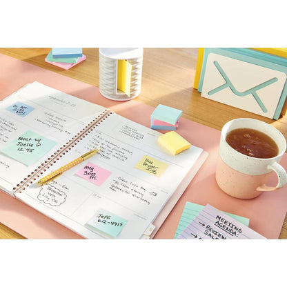 A planner with handwritten notes and 3M Post-it® Notes (38x51 mm, Yellow, 100 sheets/block, 16+4 free) lies on a desk next to a cup, a pencil, stacks of colorful sticky notes, an organizer, and note cards.