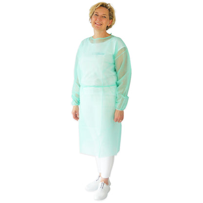 A person is standing facing forward, smiling, and wearing an ARNOMED PROTECT PP-PROTECTIVE GOWN disposable gown made of PP nonwoven by ARNOWA GmbH over white pants and shoes, against a plain white background.