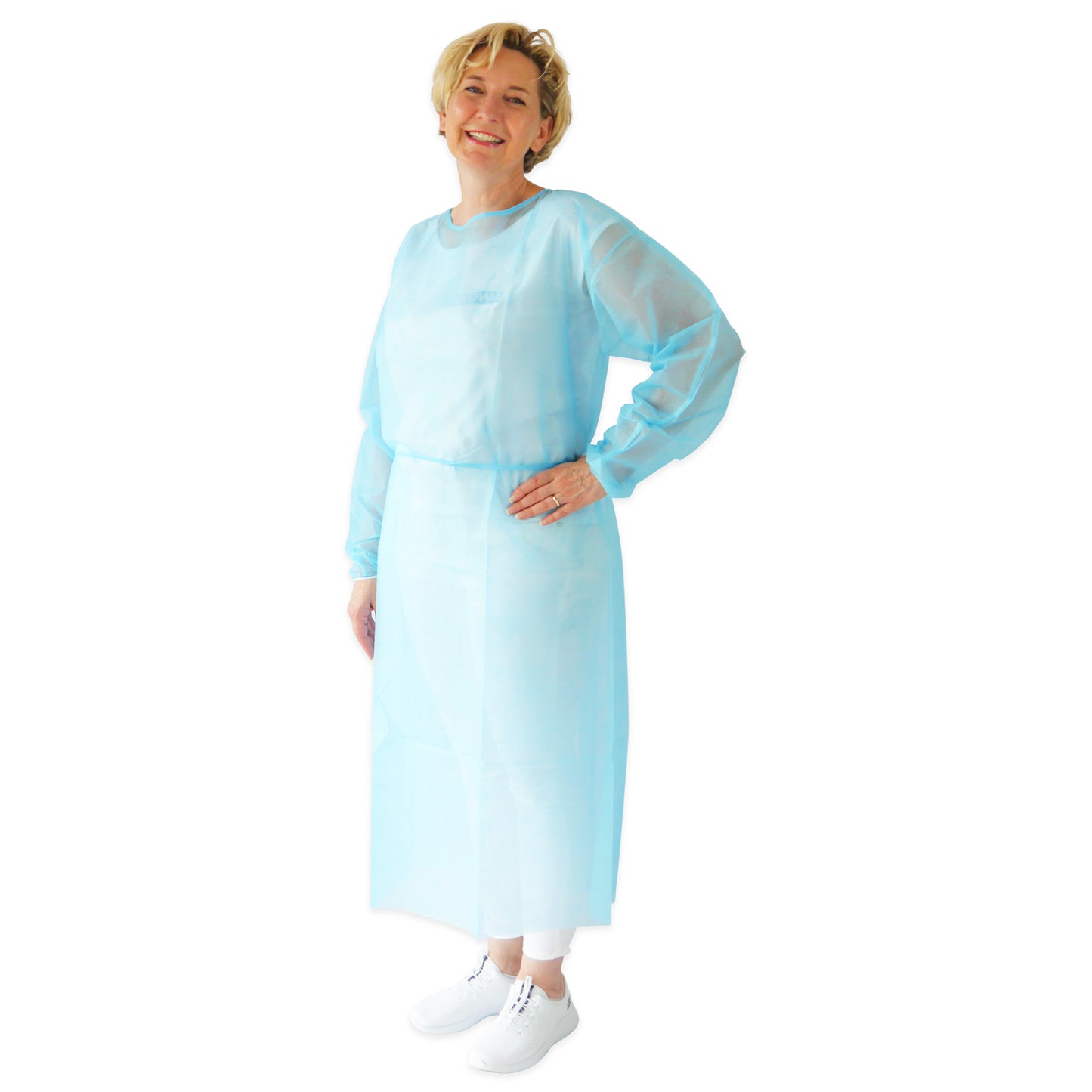 A smiling person wearing the ARNOMED PROTECT PP-PROTECTIVE GOWN disposable gown made of PP nonwoven by ARNOWA GmbH over white pants and shoes stands against a plain white background.