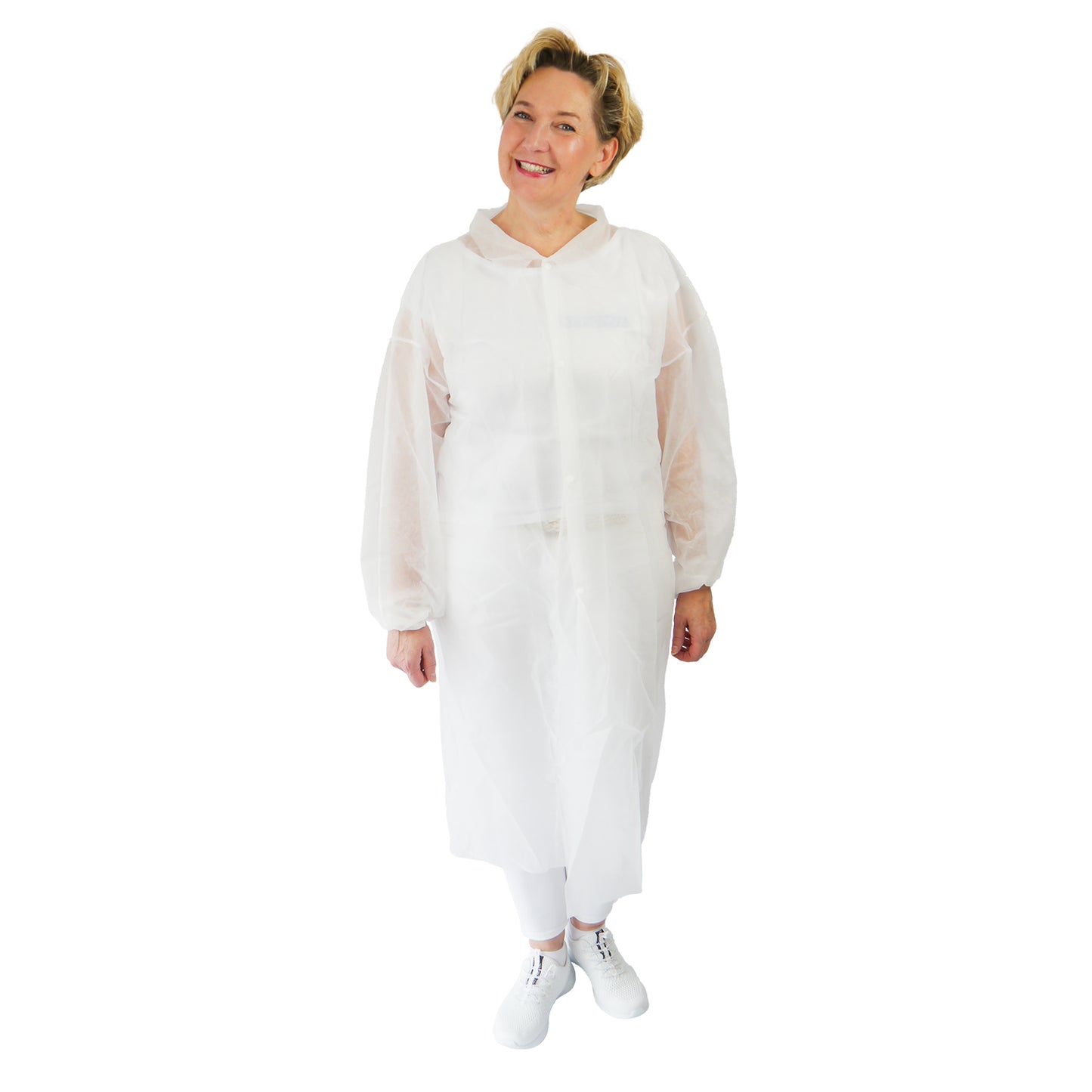 A person stands smiling and wears an ARNOMED PROTECT PP-VISITOR GOWN WHITE disposable visitor coat with snap buttons from ARNOWA GmbH, along with white pants and shoes, against a plain white background.