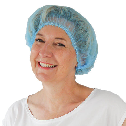 A woman in a light blue ARNOMED COVER PP CLIP CAP disposable clip cap made of PP fleece (52cm circumference) from ARNOWA GmbH and a white shirt smiles at the camera against a simple white background.