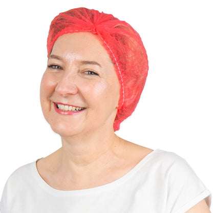 A smiling woman in a white shirt and a bright red ARNOMED COVER PP CLIP CAP disposable clip cap made of PP fleece (52 cm, ARNOWA GmbH) stands against a simple white background.